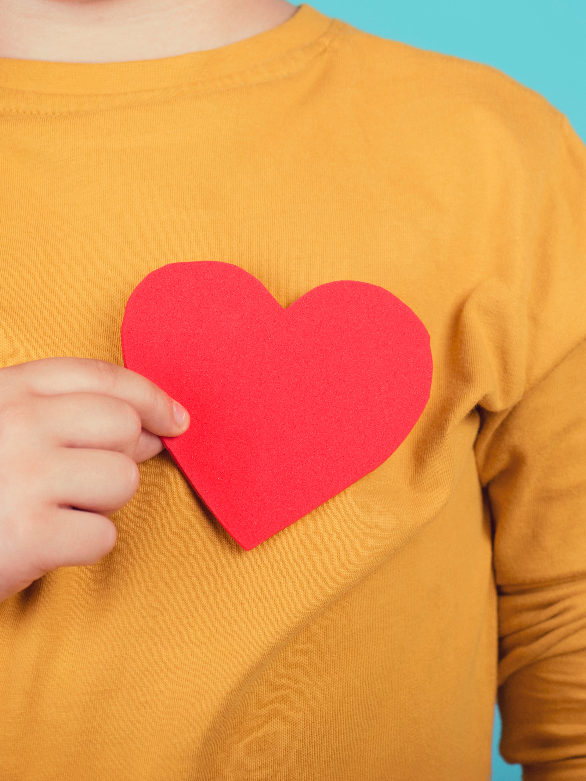 A child holds a red paper heart over their chest