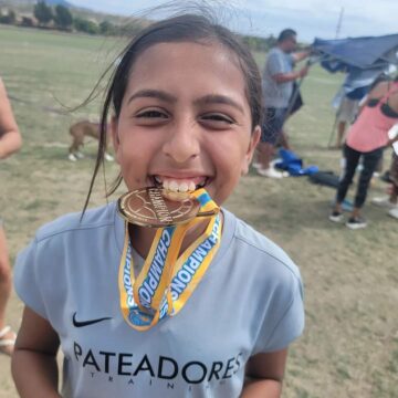Maribel's daughter holds a soccer medal in her mouth