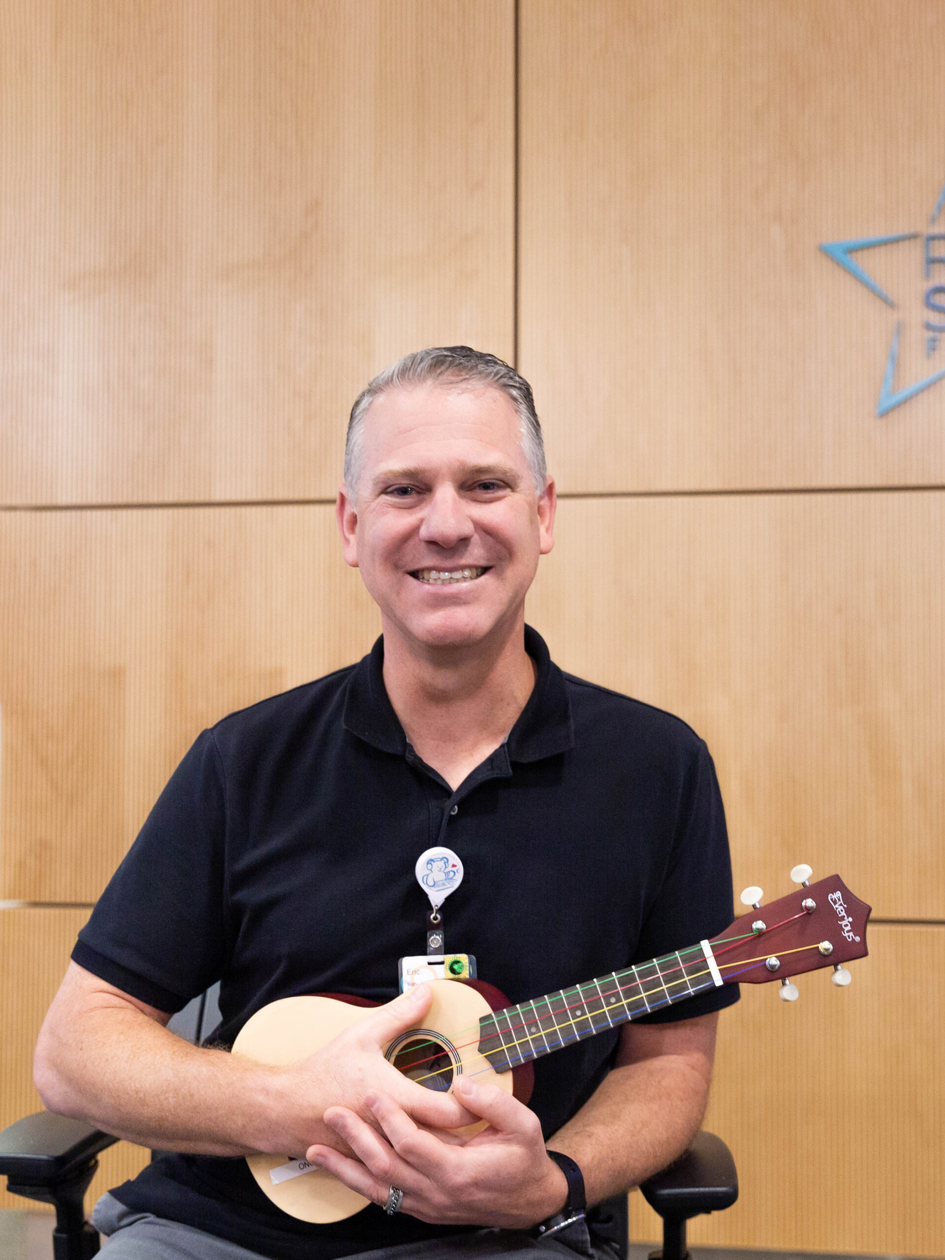 A CHOC employee in a black shirt holding a ukulele - Eric Mammen, music therapist