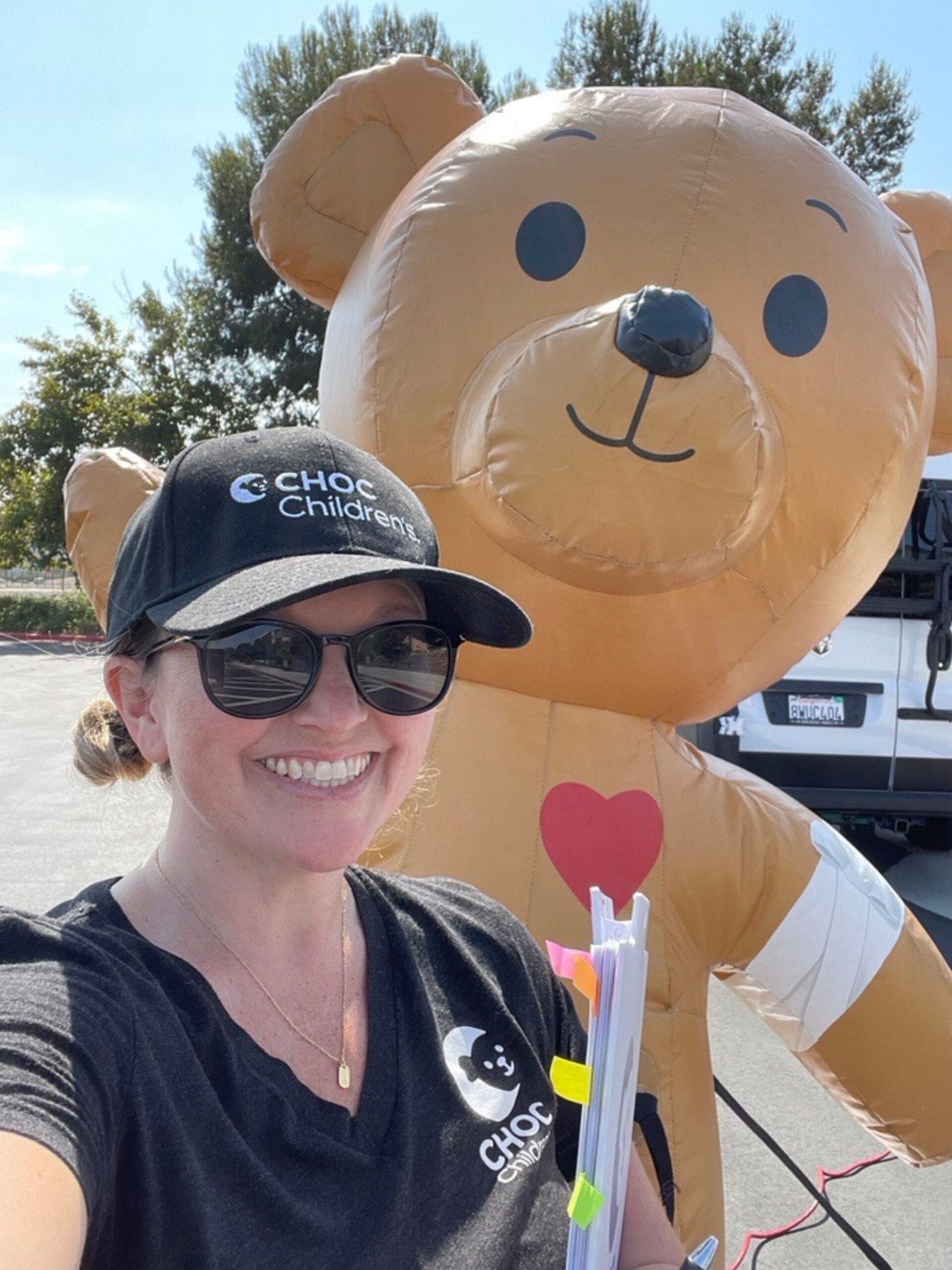 Woman in black baseball hat poses with inflatable bear - Former CHOC patient and current employee Courtney Cheney Toney