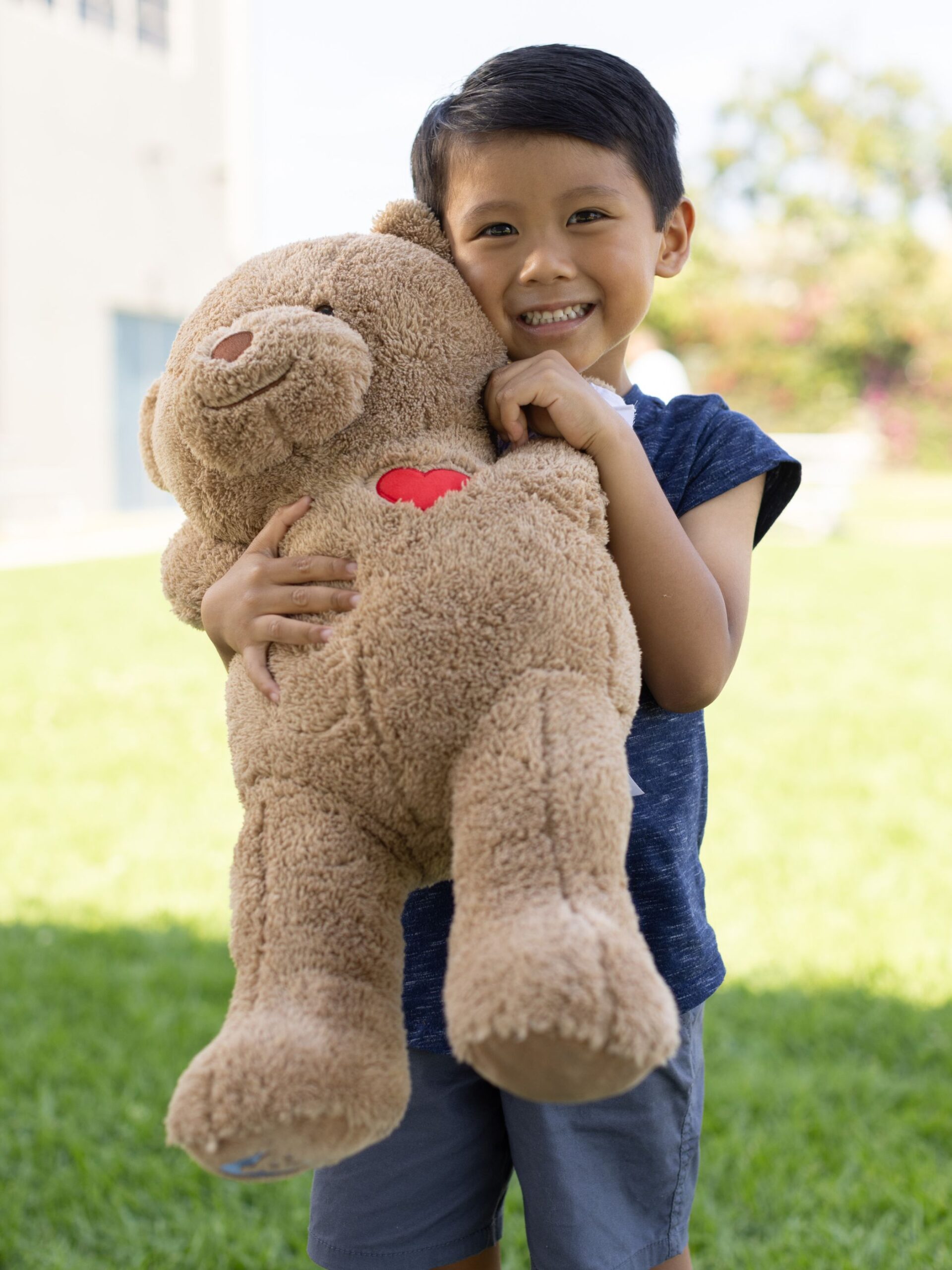 young boy with brown hair hugging large brown CHOC teddy bear.