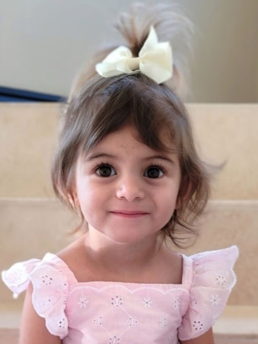 little girl with brown hair and brown eyes wearing a pink ruffle shirt and white bow in her hair - Kali, former CHOC patient and organ donor, honored at Rose Parade