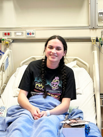 Smiling girl with dark hair in braids sits in hospital bed