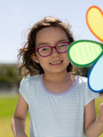 Little girl with brown hair and glasses holding a pinwheel in the shape of a flower
