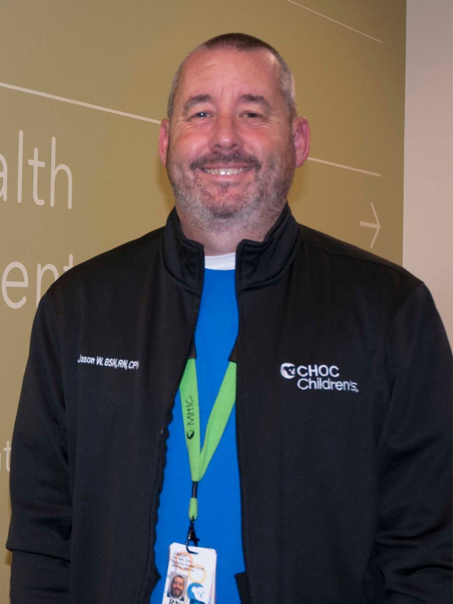 Man in black zip-up wearing blue shirt and green lanyard with badge