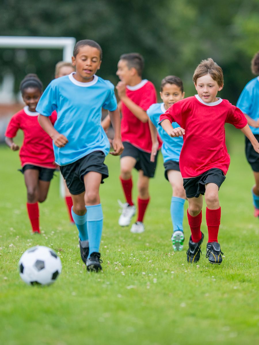 children in red and blue uniforms playing soccer outside