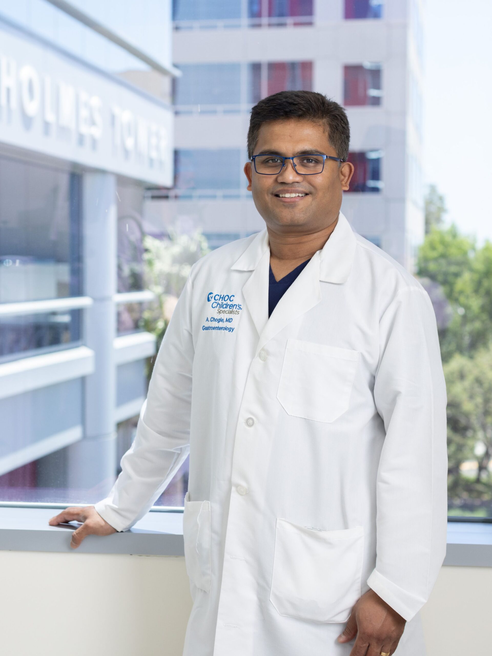 Man with glasses wearing white doctors coat poses against a window