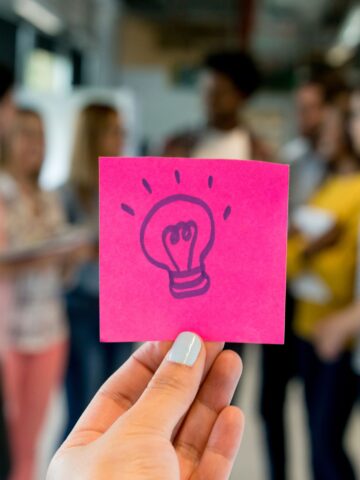 A hand holds a pink note with lightbulb drawn on it