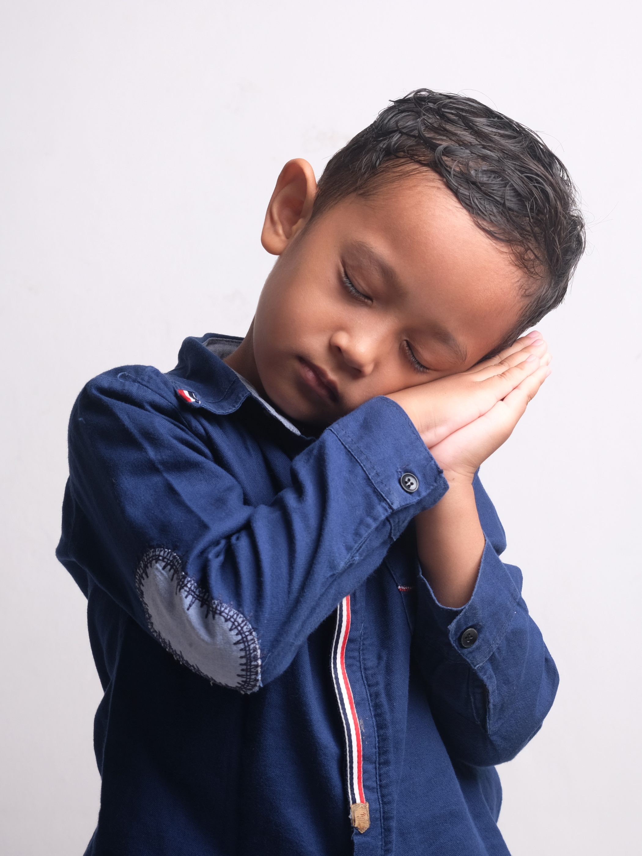 tired child with dark hair and blue shirt rest head on hands.