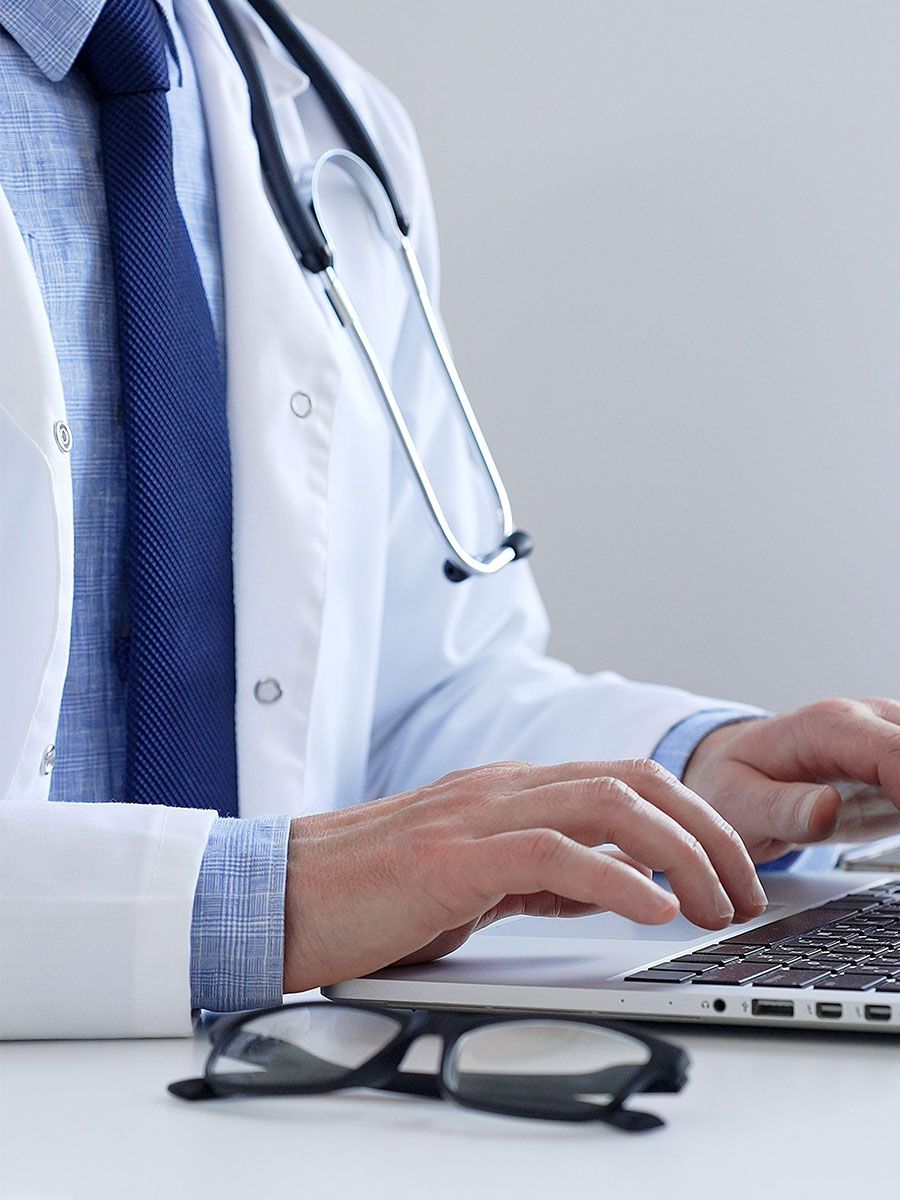 Medical professional typing on laptop, updating electronic patient records with focused concentration, representing digital transformation in healthcare workplace